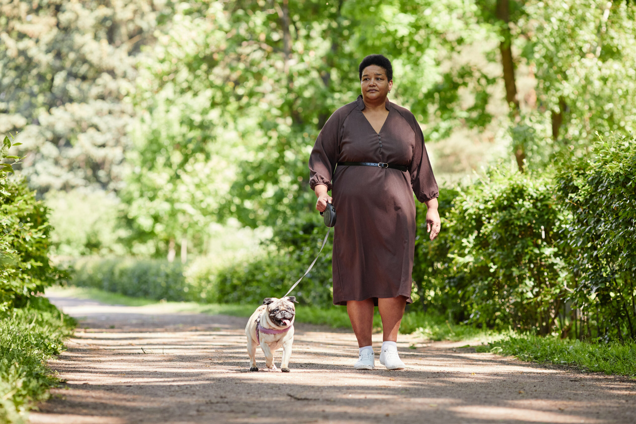 Larger woman on sunny forest path, walking her dog